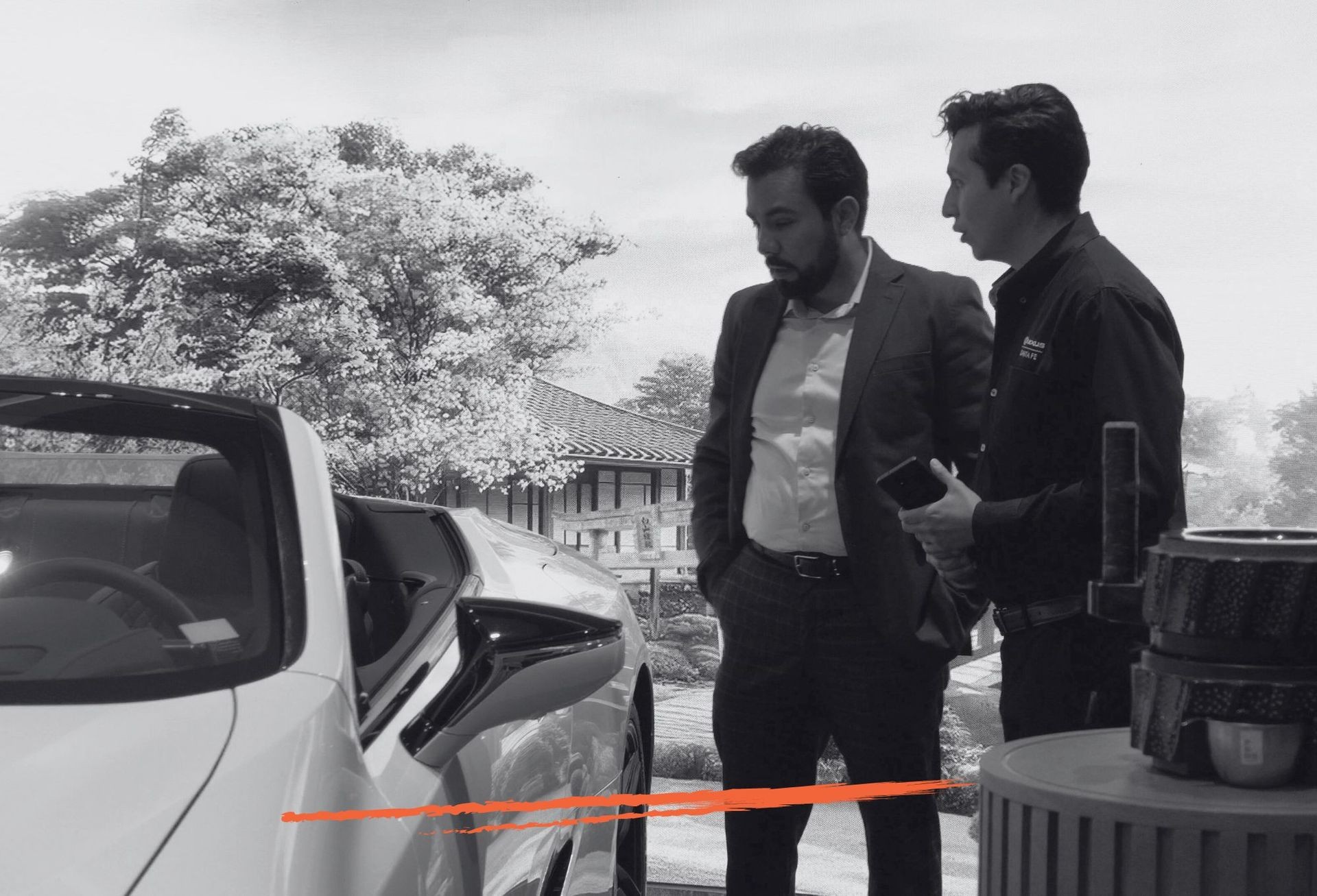 Two men standing beside a white sports car with a traditional building in the background.