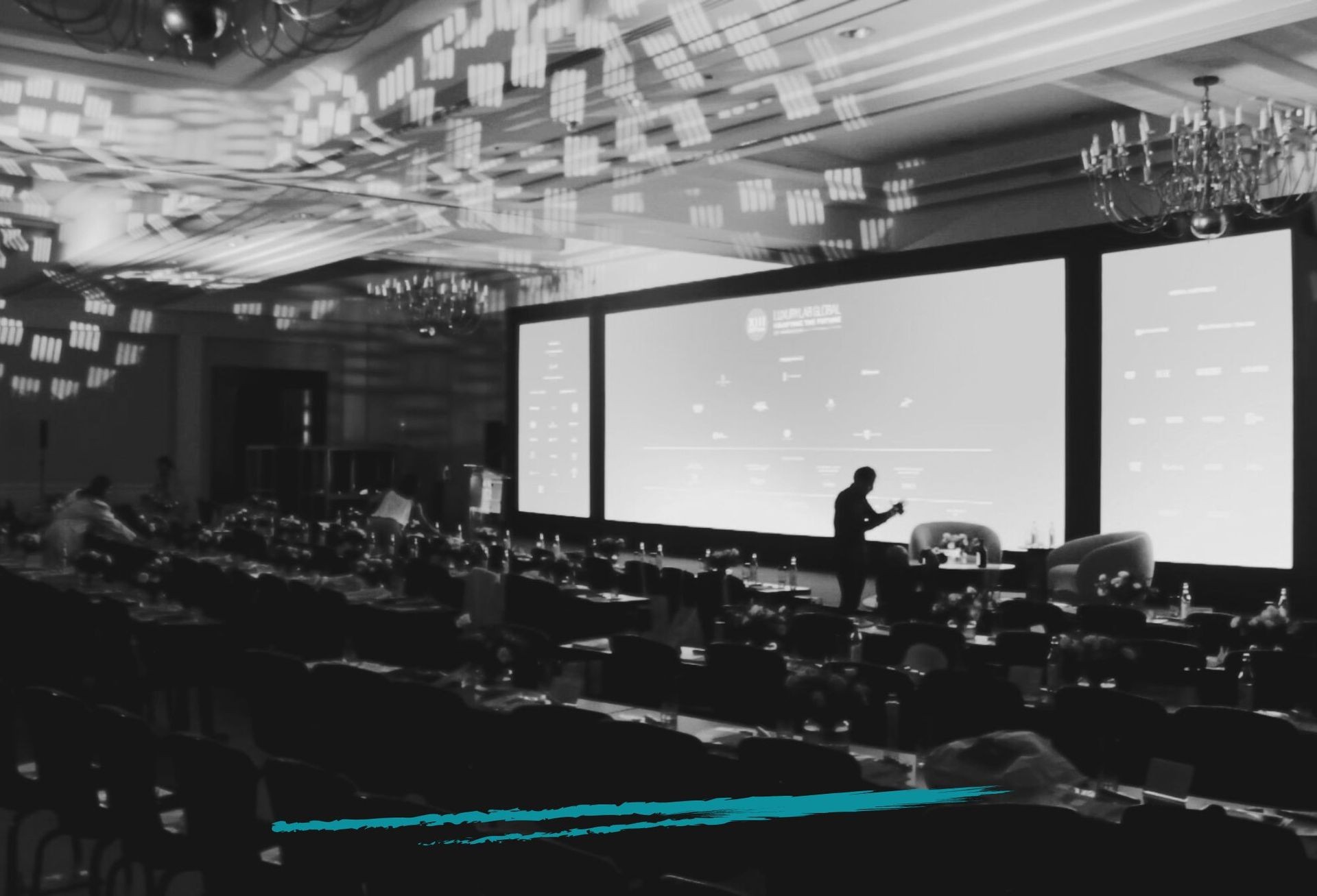 Black and white photo of a conference room with large screens and silhouetted people preparing the space.